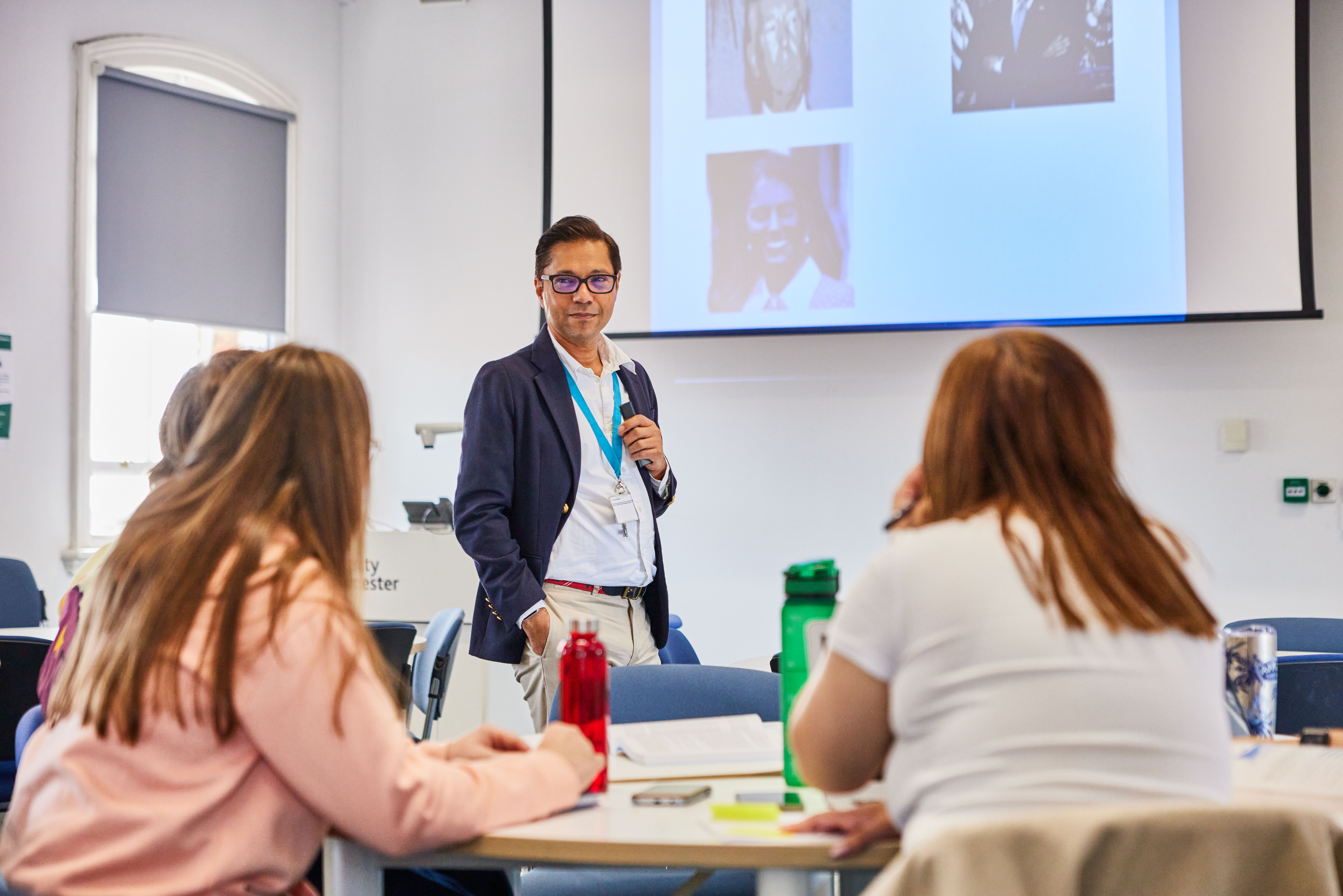 A lecturer stands at the front of the class looking at his students who are sat down listening