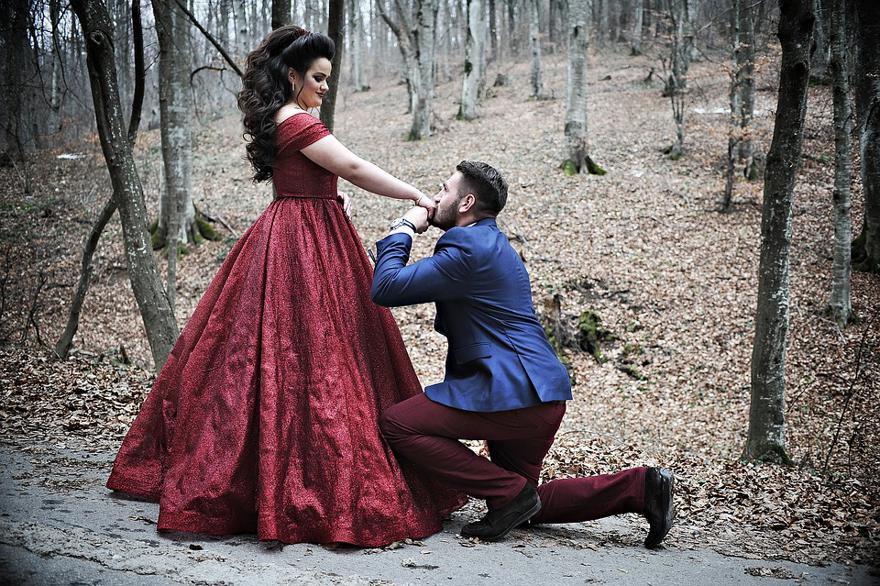 Man kissing the hand of a woman in a red dress while in the woods