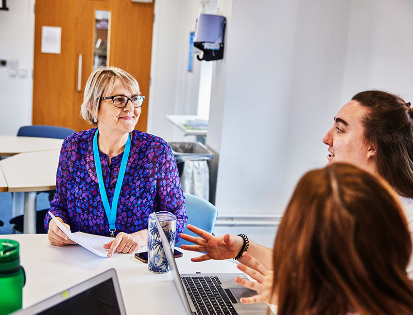 Lecturer sat a table with her students listening to them