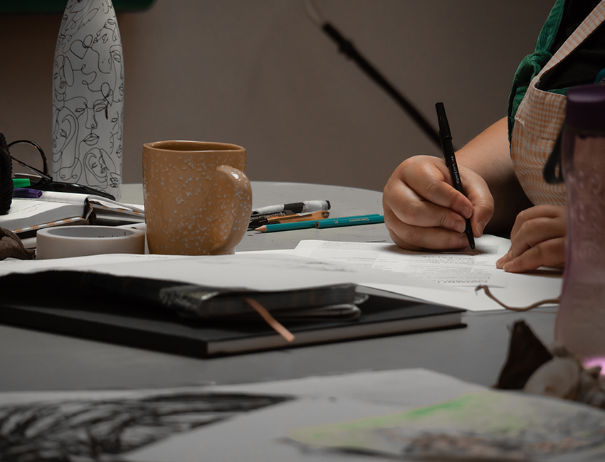 Hands sketching on a desk with notepads and pens