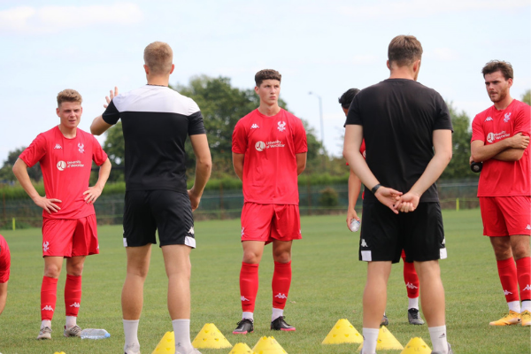 Footballers in red kit with the University of Worcester logo engage in a coaching session