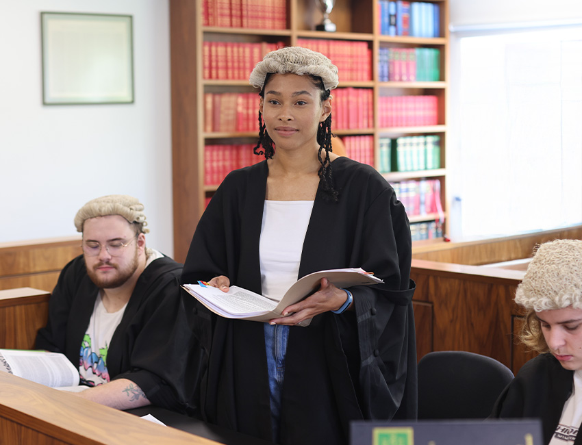 A law student in traditional wig and robe standing in a courtroom.