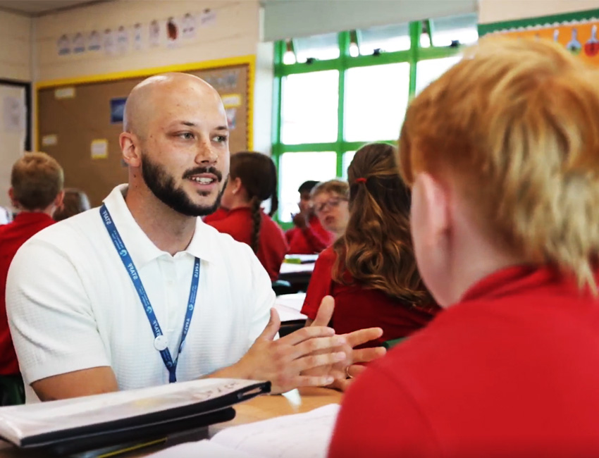 Male teacher speaking to two of his pupils at their desks