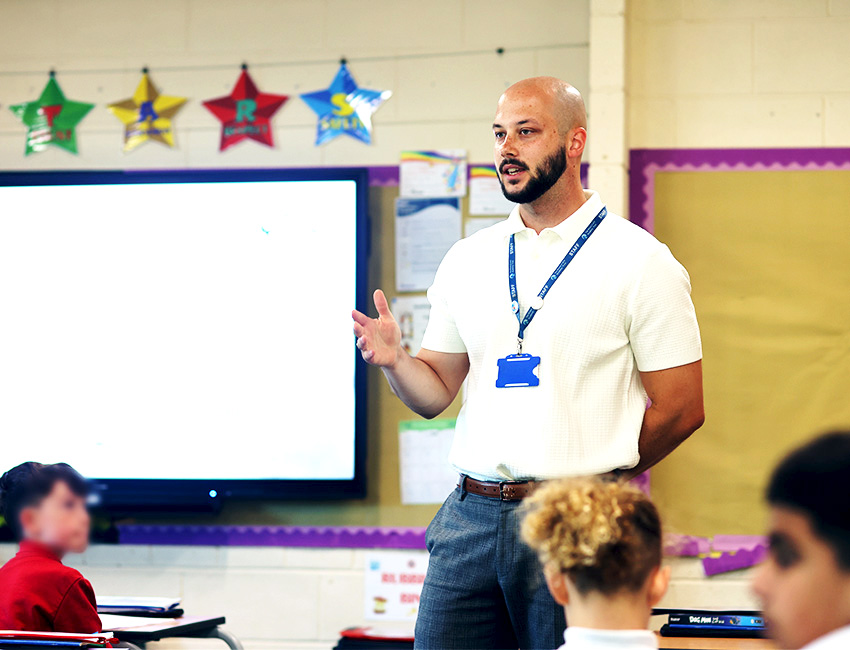 Male teacher stood at the front of a primary school classroom teaching