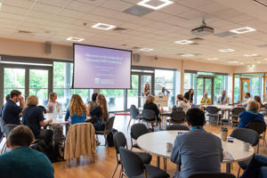 The PGR conference, with attendees seated around round tables and a welcome screen on display at the front of the room.