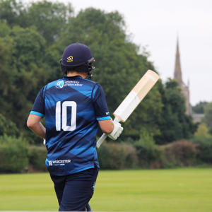 A student playing cricket on a pitch outside