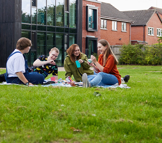 Four students having a picnic on the lawn outside the Mary Seacole building