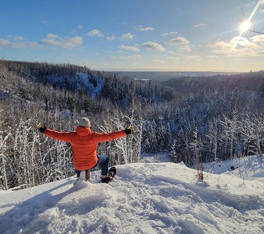 A student siting on a snowy hill overlooking a forest