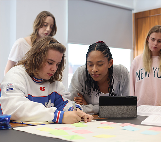 A group of four students gathered around a table and looking and notes