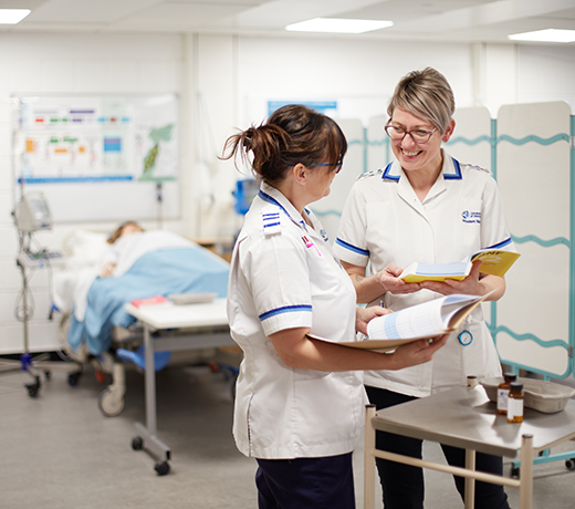 Two nurses discussing their notes in a hospital ward