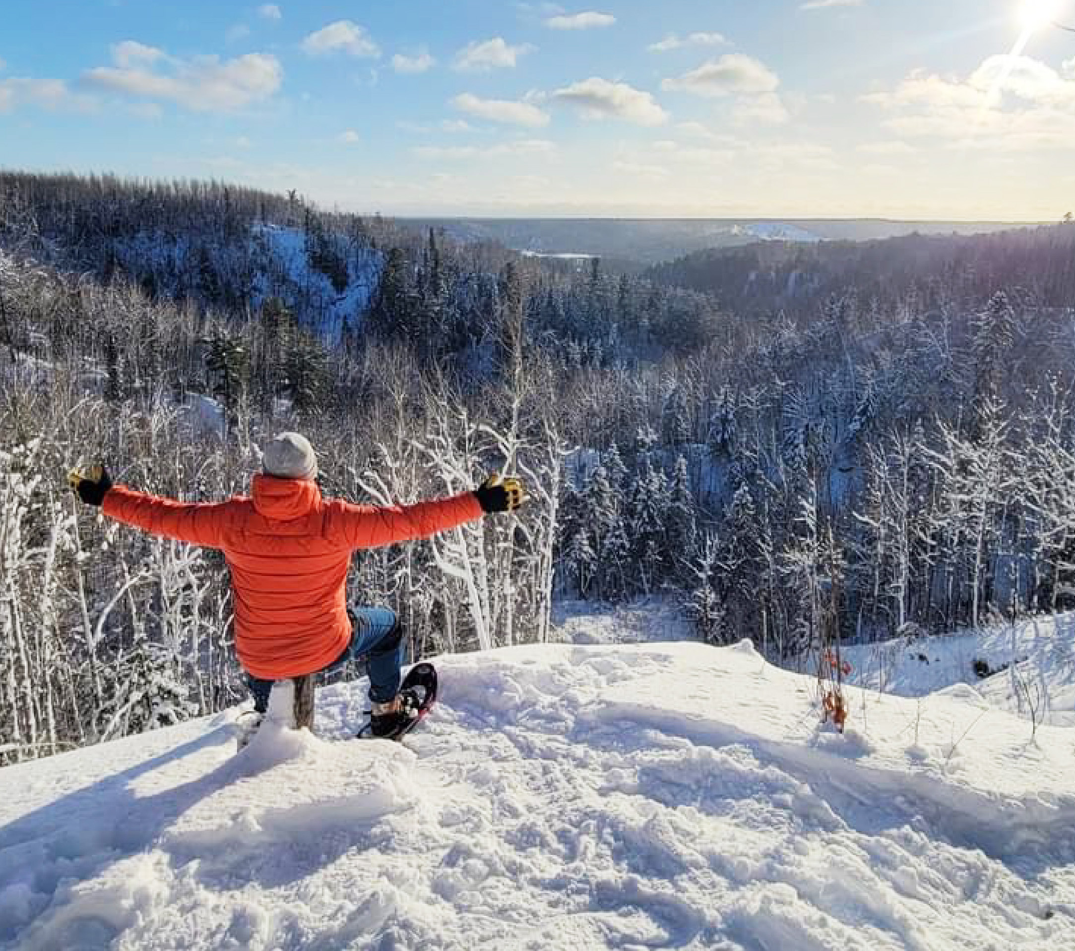 A student siting on a snowy hill overlooking a forest