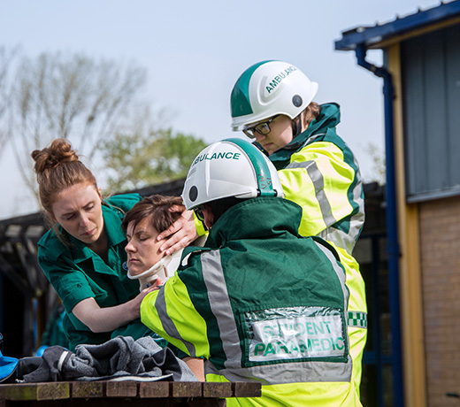 Three student paramedics practicing supports for head and neck injuries on another student