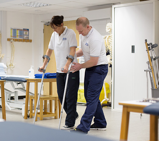 A physiotherapy student assisting another student using crutches