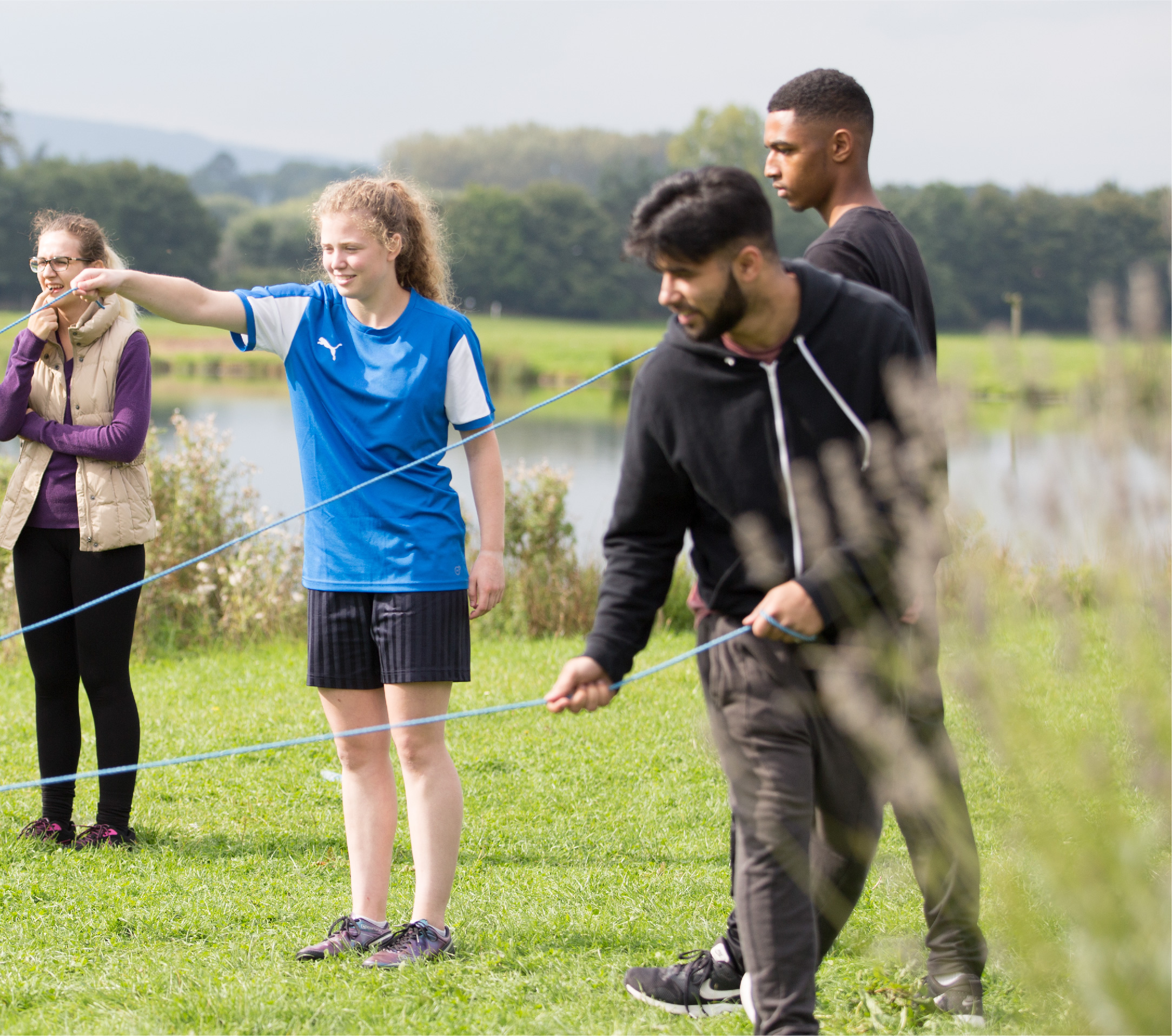 A group of four students taking part in a team building activity beside a lake