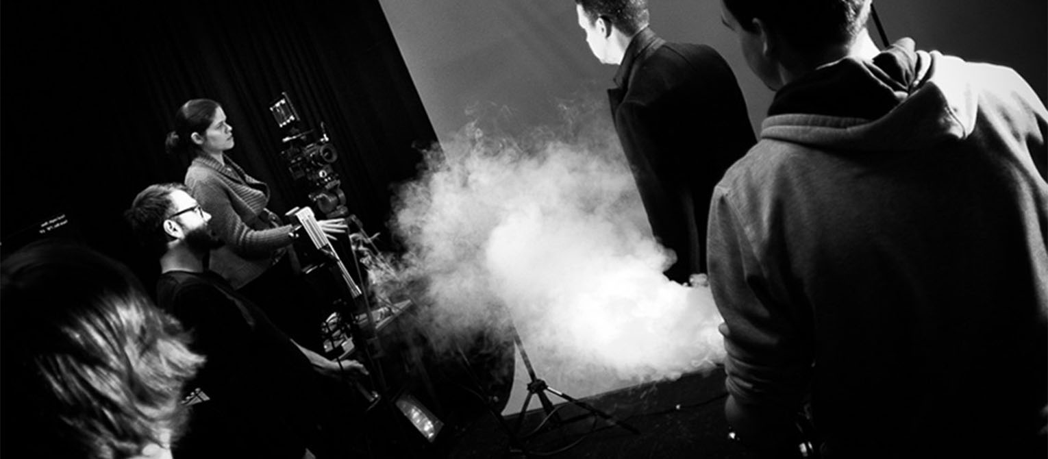 Black and white image of students filming smoke against a green screen.