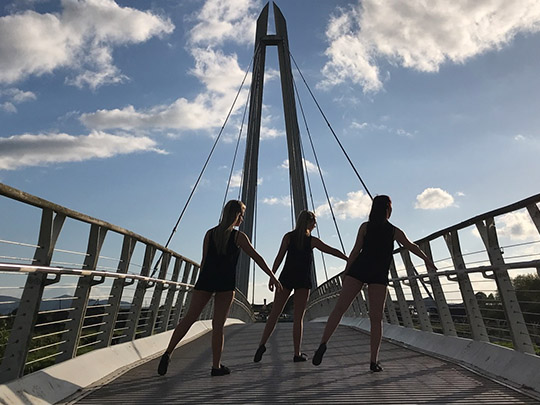 Three dancers on footbridge silhouetted against blue sky