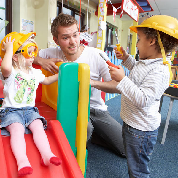 Children dressing up as construction workers with male nursery practitioner