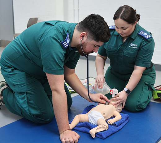 Two paramedic students measuring the heartbeat of an infant medical manikin