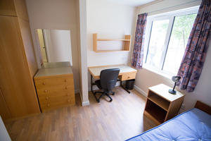 inside a well-lit bedroom including a window a cupboard and the edge of a bed