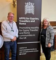 Two members of staff at the House of Commons, beside a banner reading: "APPG for Gypsies, Travellers and Roma"