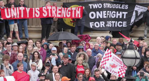 A protest with people holding up signs reading: "unity is strength" and "two struggles, one fight for justice"