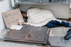 A homeless person sleeping on the street next to a sign reading: "homeless and hungry"