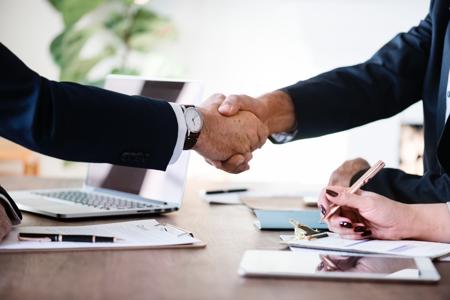 A close up shot of two people's arms shaking hands at a table