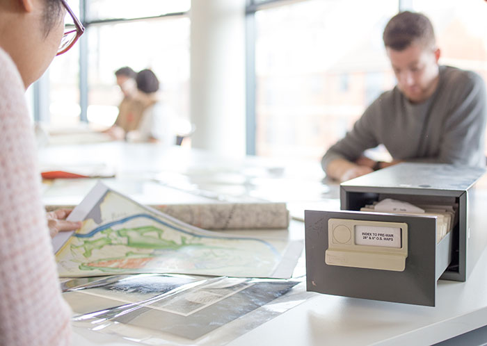 Two students are looking at historical maps in the library