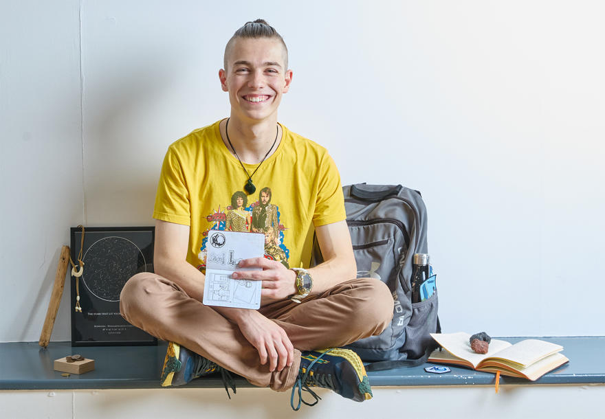 A young person wearing a yellow Abba t-shirt sitting and smiling