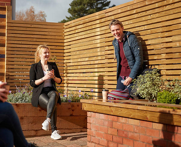 A group of mature students are standing outside and drinking coffee